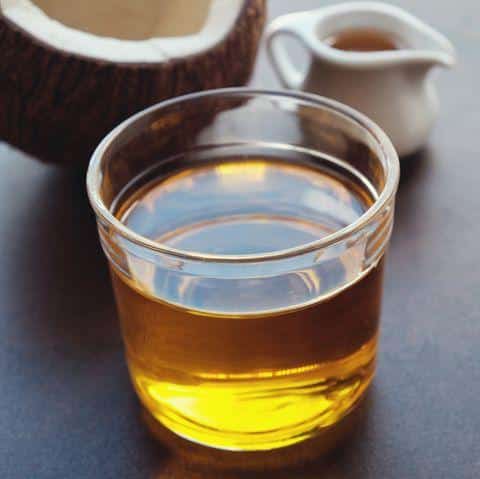 a glass of oil next to a coconut on a table.